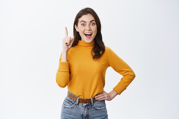 I got it Excited brunette girl having an idea raising finger in eureka sign and smiling amazed say suggestion standing against white background