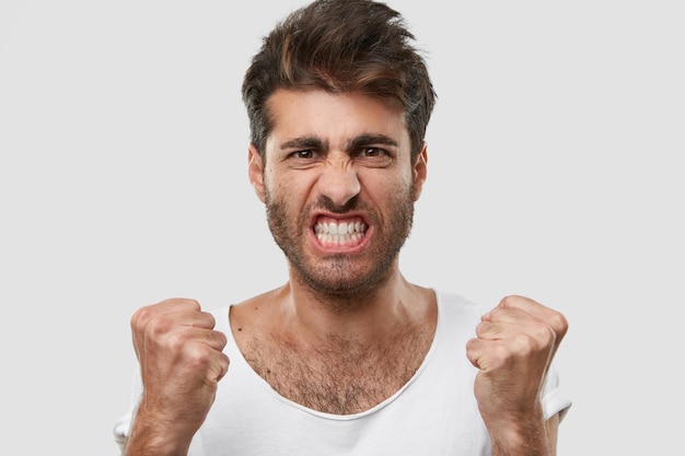 I hate tihs idea! Close up shot of annoyed unshaven man with trendy hairstyle, clenches teeth, raises fists, looses temper