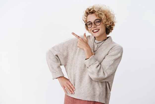 I have just what you need Assured and friendlylooking enthusiastic charming blond female in glasses and sweater smiling and gazing selfassured at camera as pointing at upper left corner