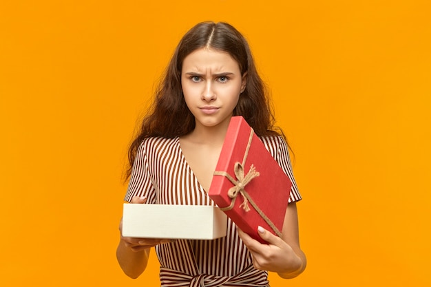 I don't like it. Isolated shot of displeased stylish young woman with wavy hair opening box