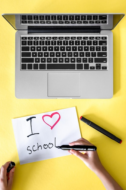 Foto gratuita adoro la scuola la mano del bambino scrive su un giornale su uno sfondo giallo