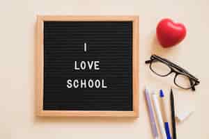 Free photo i love school text on slate near pens; eraser; eyeglasses and red heart over plain background