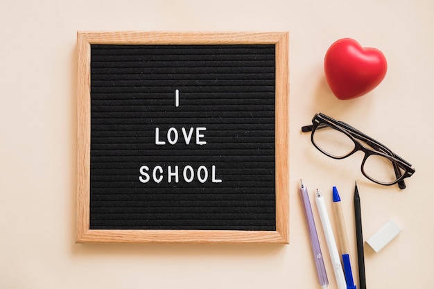 I love school text on slate near pens; eraser; eyeglasses and red heart over plain background