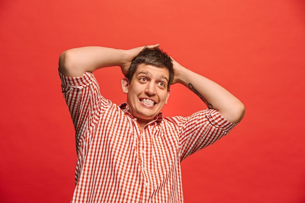 Free photo i'm afraid. fright. portrait of the scared man. business man standing isolated on trendy red studio background. male half-length portrait.  front view