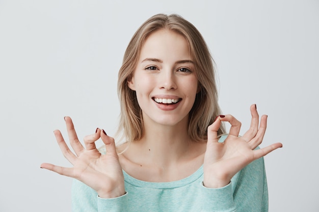 잘하고 있어요 파란색 스웨터 넓게 웃 고 양손으로 좋은 제스처, 기쁨 좋은 하루, 인생 목표, 업적 확인 제스처를 만드는 다행 행복 젊은 금발 여성. 신체 언어. 기쁨과 행복.