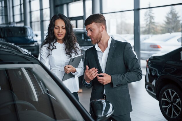 私はその新しい車にとても感銘を受けました。女性客と自動車サロンでモダンなスタイリッシュなひげを生やした実業家