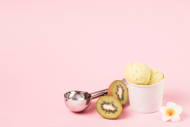 Ice cream balls in cup near kiwi with scoop and flower