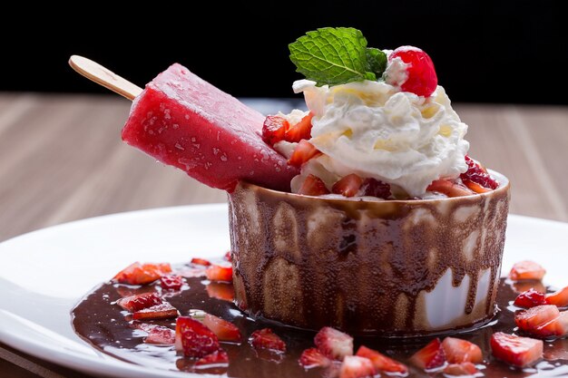 Ice cream in a bowl of dessert with chocolate, cream and strawberries