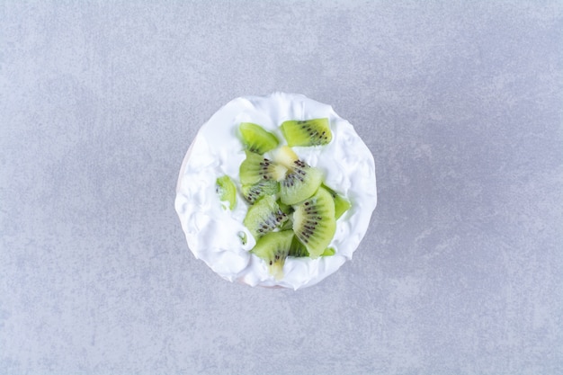 Ice cream in a glass pedestal with slices kiwi on marble table.