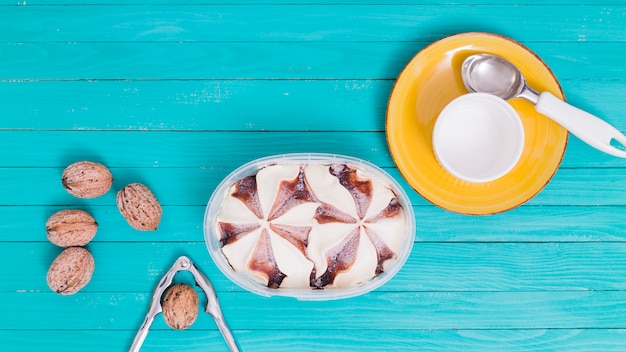 Free photo ice cream in plastic bowl and yellow plate with cup and spoon and walnuts with nutcracke