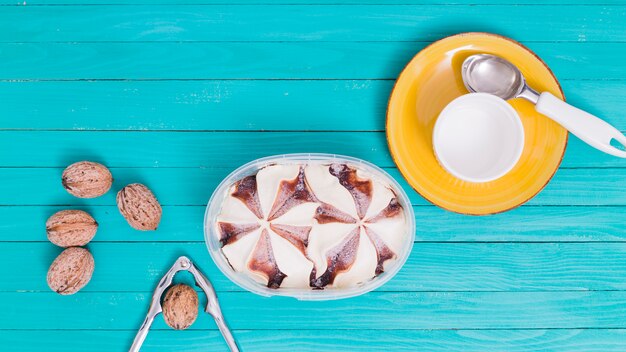 Ice cream in plastic bowl and yellow plate with cup and spoon and walnuts with nutcracke