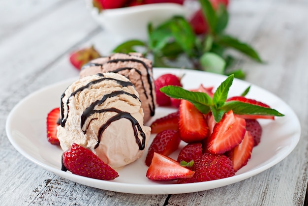 Ice cream with strawberries and chocolate on a white plate