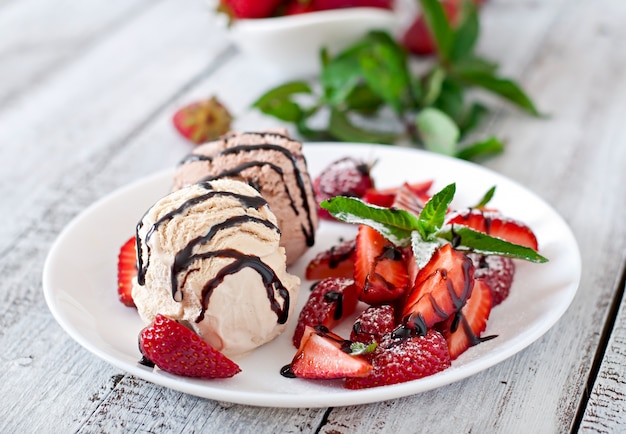 Ice cream with strawberries and chocolate on a white plate