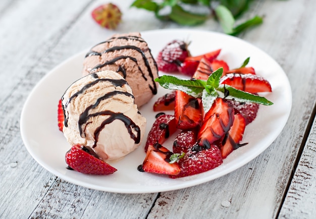 Ice cream with strawberries and chocolate on a white plate