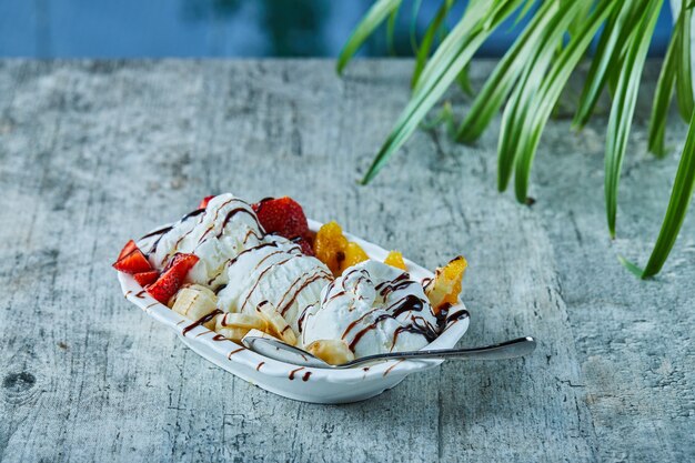 Ice-cream with strawberry, banana, orange on the white plate with spoon