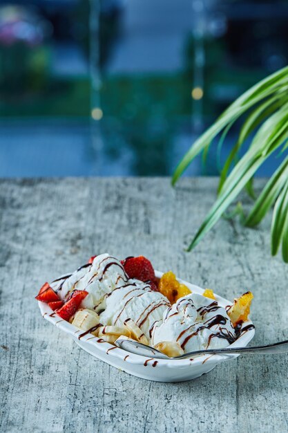 Ice-cream with strawberry, banana, orange on the white plate with spoon