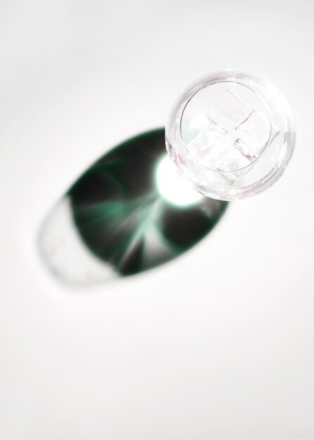 Ice cubes in transparent wineglass with dark shiny shadow on white backdrop