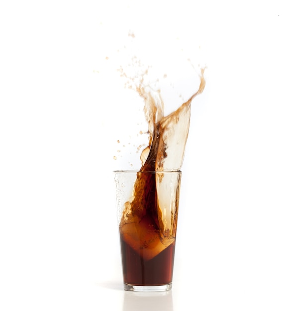 Ice falling into a glass with brown drink
