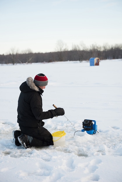 Foto gratuita pescatore sul ghiaccio pesca nel paesaggio innevato