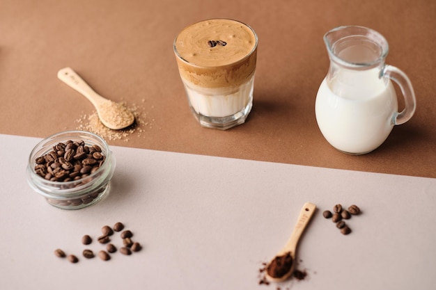 Кофе далгона со льдом с миндальным молоком и кофейными зернами с коричневым сахаром на бежевом листе стакан модных пушистых взбитых сливок koreith