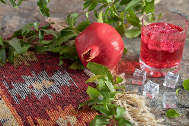 Foto gratuita succo ghiacciato e melograno con foglie e tappeto sulla superficie della pietra