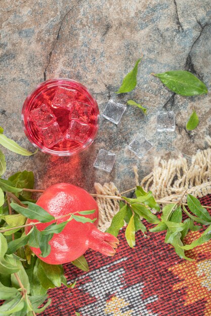 Iced juice and pomegranate with leaves on stone surface