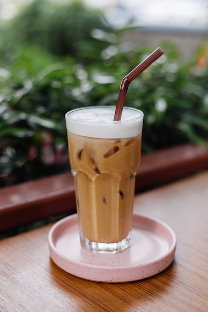 Iced latte in glass on a pink stand on wooden table in summer cafe green bushes