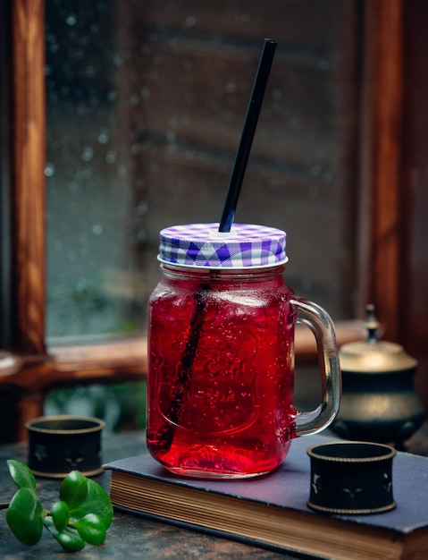 iced pink drink in mason jar with black straw in front of the window