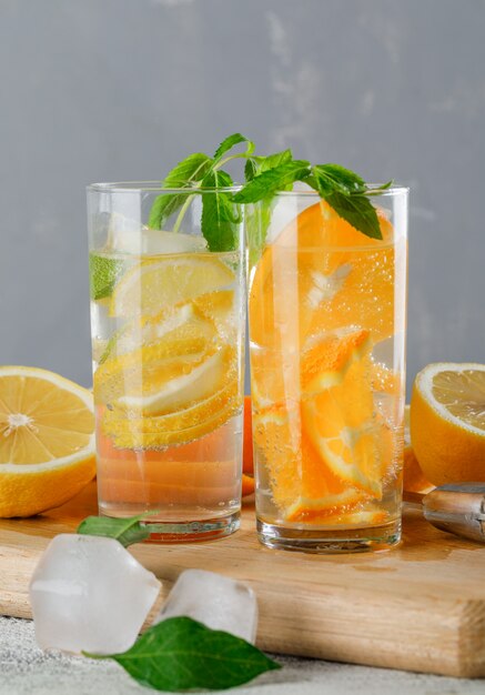 Icy detox water in glass with orange, lemon, mint, cutting board close-up on grunge and grey wall