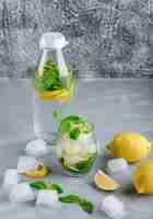 Free photo icy detox water with lemons, mint in glass and bottle on grey and grungy surface