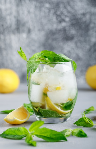 Icy detox water with lemons and mint in a glass on grunge and grey surface