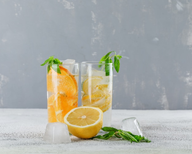 오렌지와 레몬, 석고와 그런 지 배경, 측면보기에 유리에 민트와 얼음 해독 물.