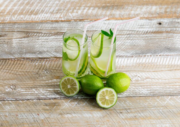 Icy lemonade in glasses with lemon, basil flat lay on a wooden