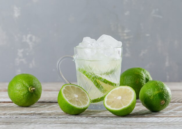 Icy mojito cocktail in a cup with limes side view on wooden and plaster background