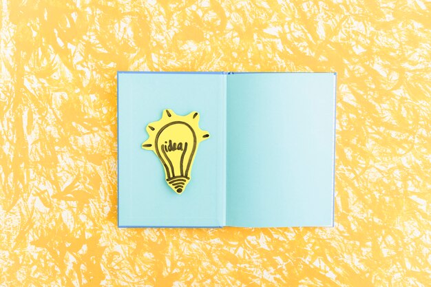 Idea light bulb on blue page notebook over the yellow textured background