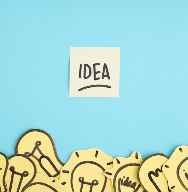 Idea text on sticky note over the different yellow light bulbs on blue background