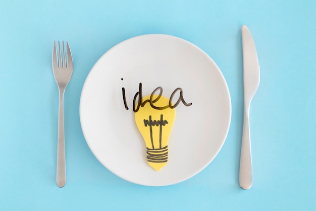 파란색 배경에 포크와 버터 나이프와 하얀 접시 위에 노란 전구와 아이디어 텍스트