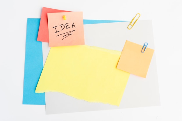 Idea text written on sticky note with pushpin and paperclip on white board