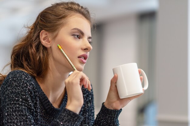 Ideas for business. Studying and working at home. Thoughtful young woman making notes using notepad in kitchen.