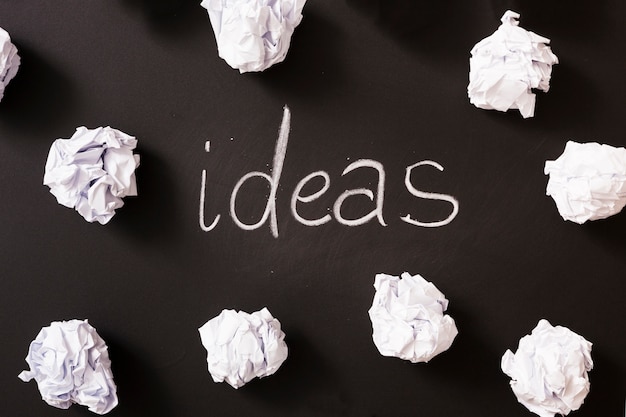 Ideas word surrounded with white crumpled paper balls on blackboard