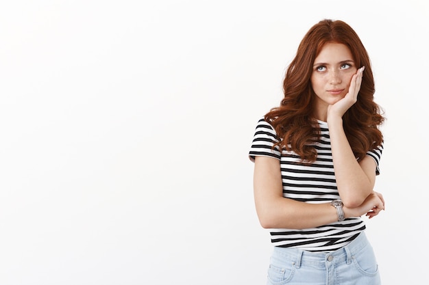 Ignorant indifferent redhead teenage girl in striped t-shirt rolling eyes up bothered and annoyed with lame pick-up line, lean face palm, smirk with disdain and contempt, standing white wall