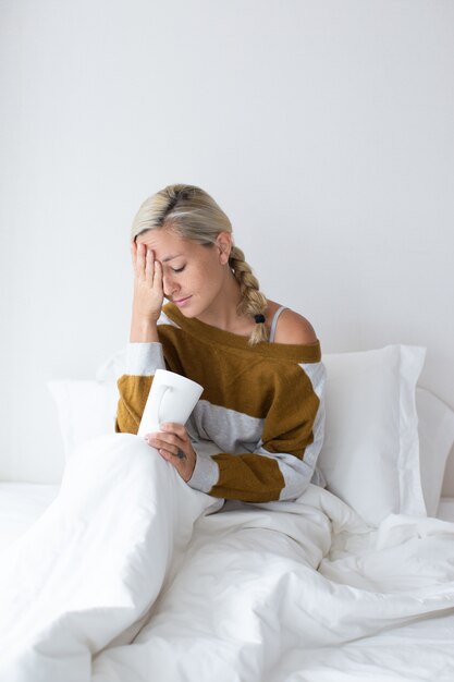 Ill woman sitting on bed and touching forehead