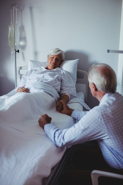 Ill woman sleeping on bed while worried man sitting beside her bed