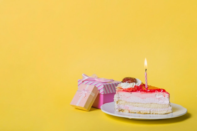 Свеча свечи на ломтик торт с двумя подарочные коробки на желтом фоне