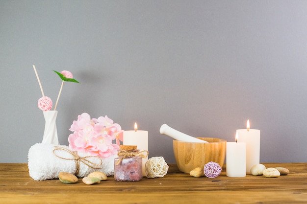 Illuminated candles; scrub bottles; flower; spa stones; mortar and pestle on wooden tabletop