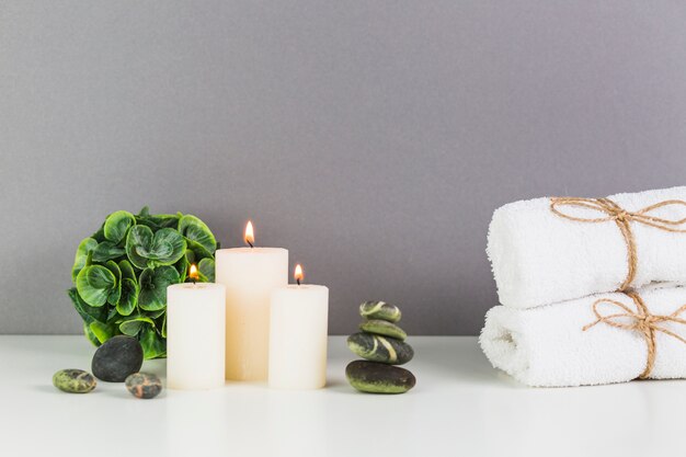 Illuminated candles; towel and spa stones on white tabletop