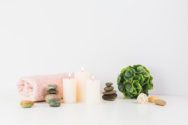 Illuminated candles; towel; spa stones on white tabletop