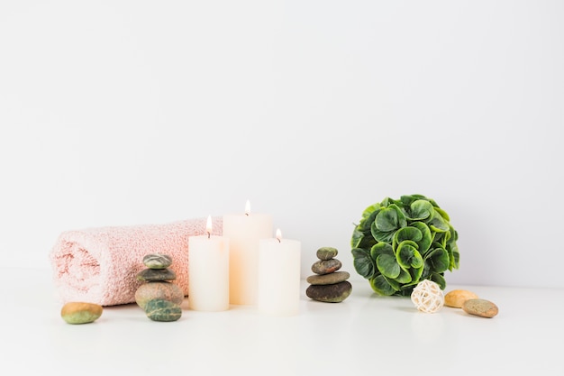 Illuminated candles; towel; spa stones on white tabletop