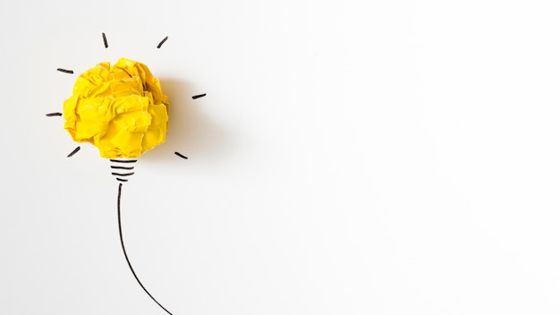 Illuminated crumpled yellow paper light bulb idea on white background