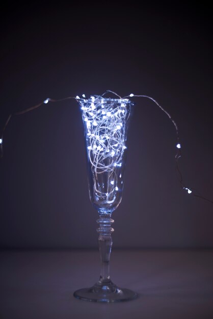 Illuminated fairy light in transparent champagne glass on dark background